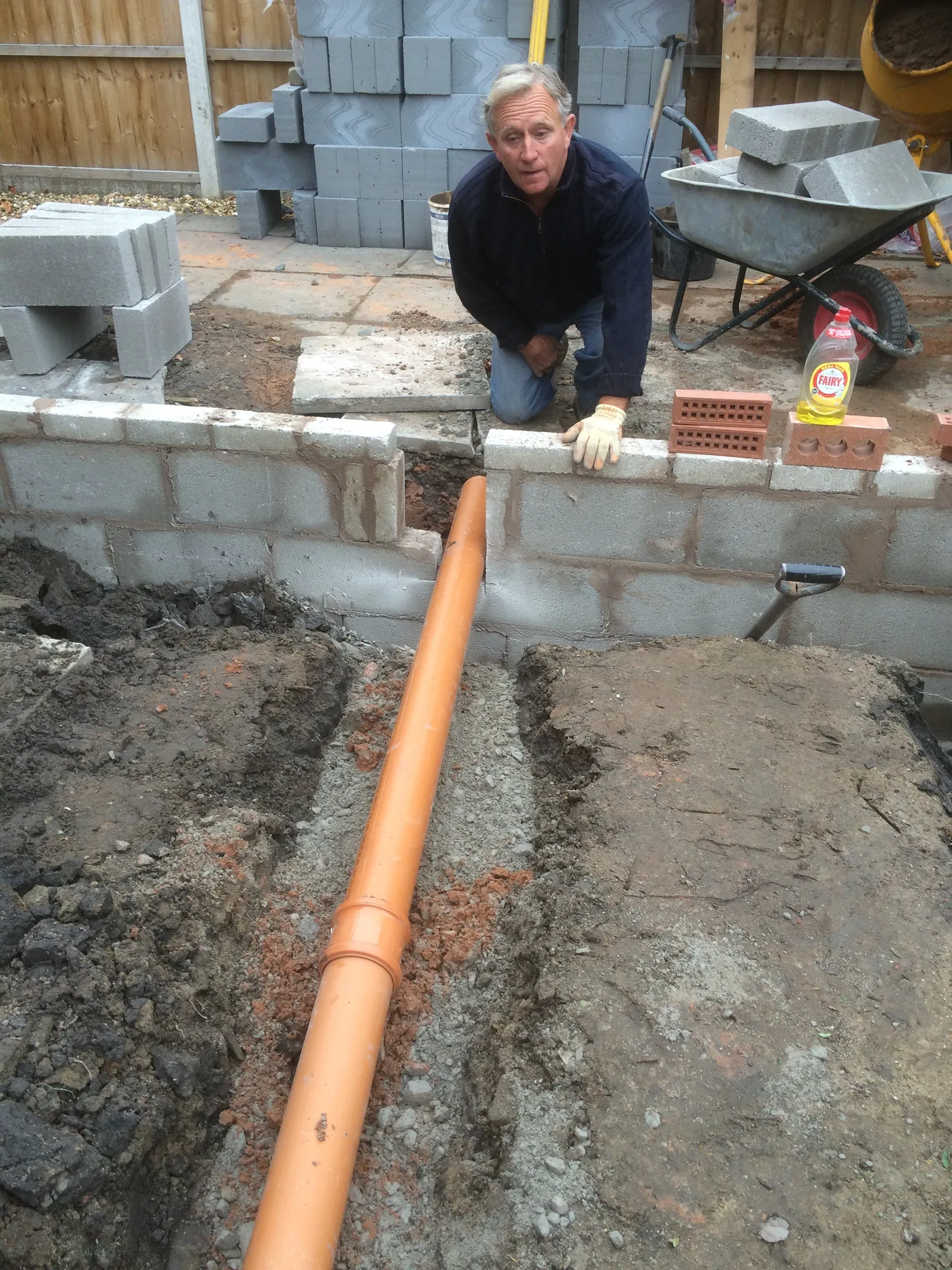 Blockwork and facing brickwork being built off a new footing alongside a drainage run.