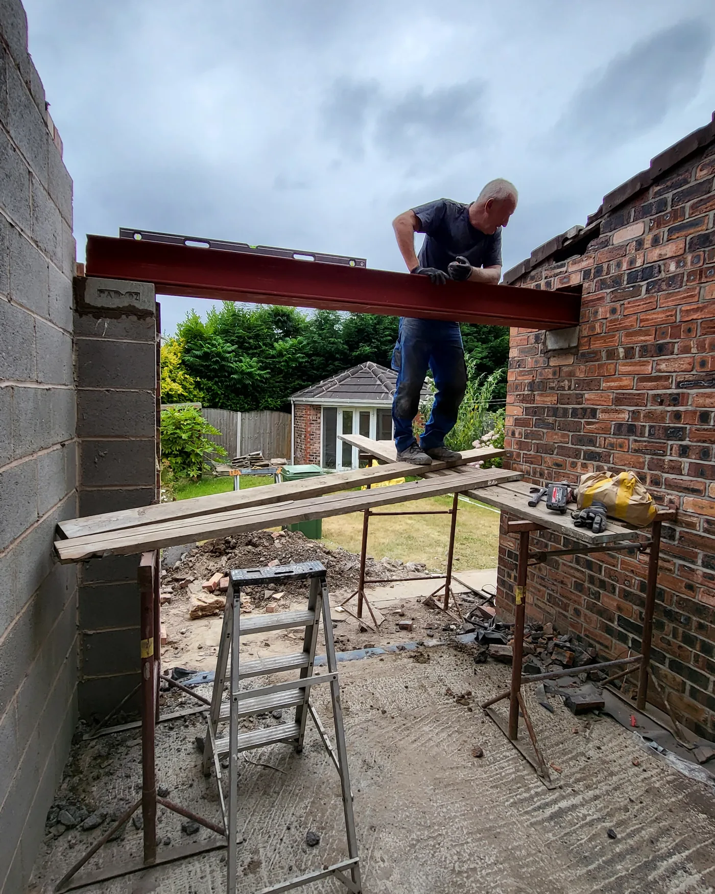 A structural steel beam being set into position on brick padstones during an extension build.