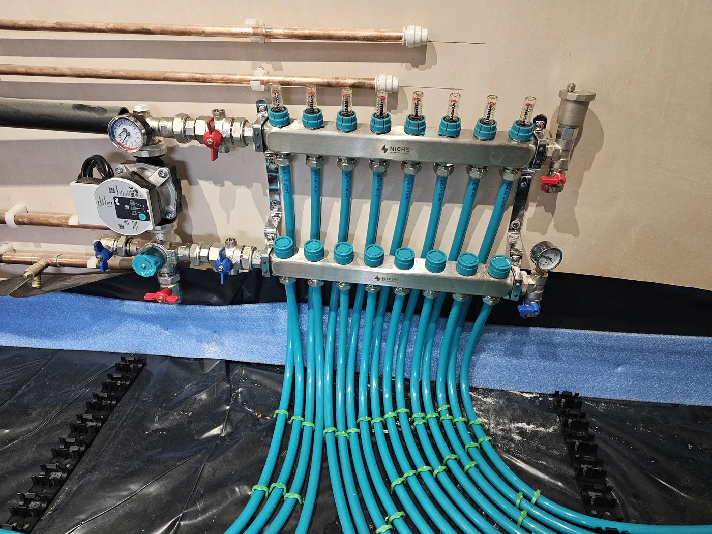 Underfloor heating manifold with colour-coded circuits and pipework fanning out across an insulated floor.
