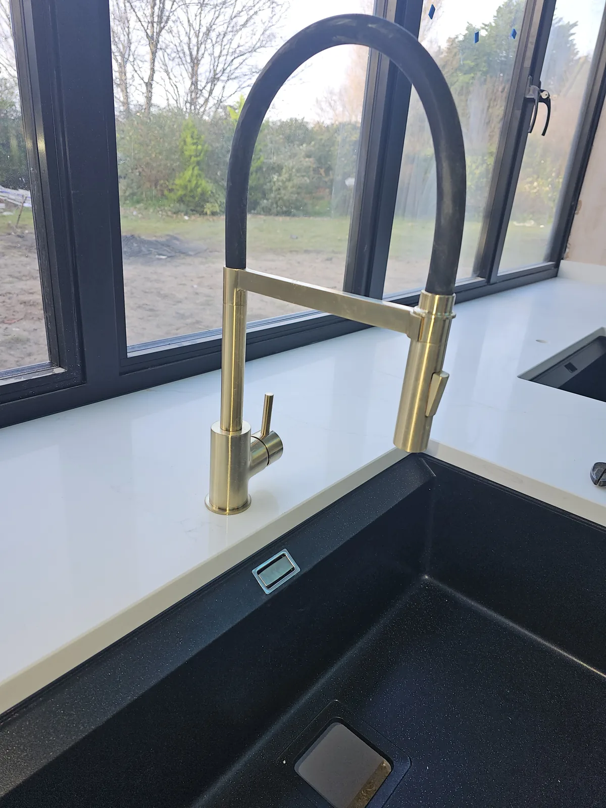 Brushed brass mixer tap over an undermounted black sink set into a dark stone worktop.