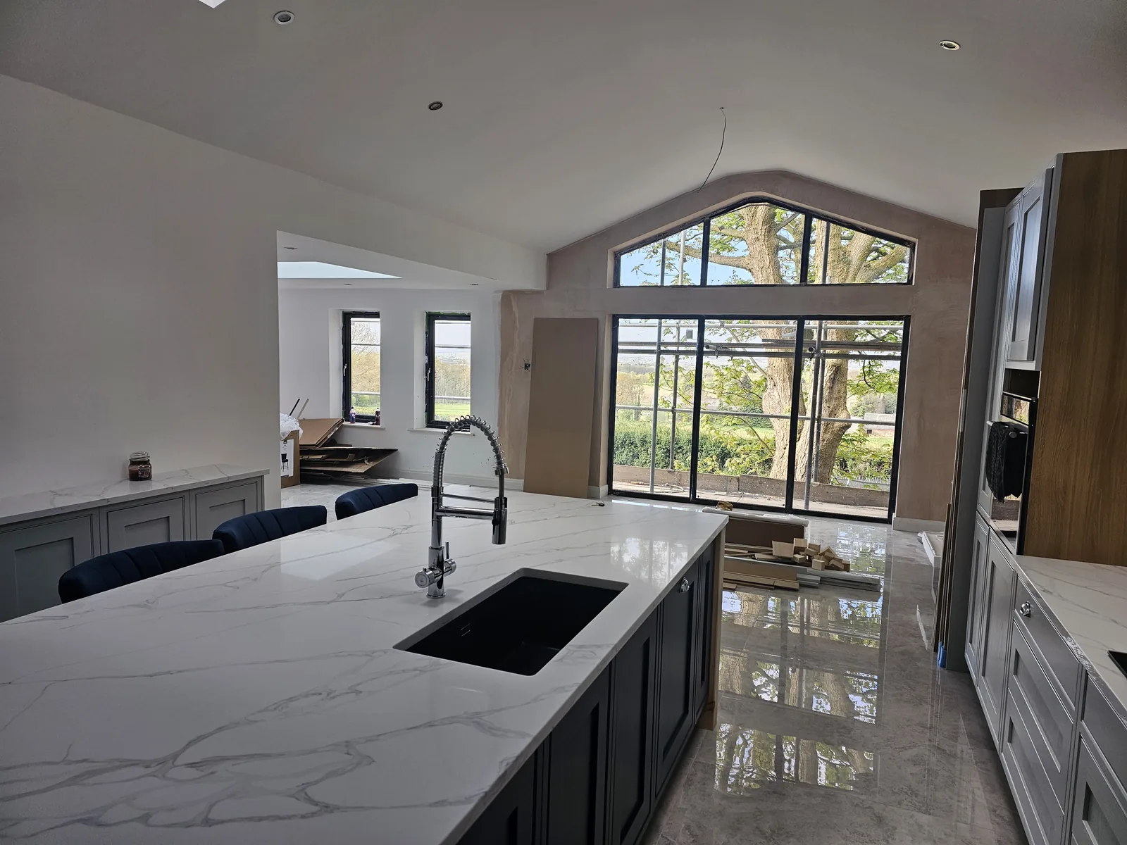 Kitchen with an arched black steel-framed window, marble-effect waterfall island and dark cabinetry.