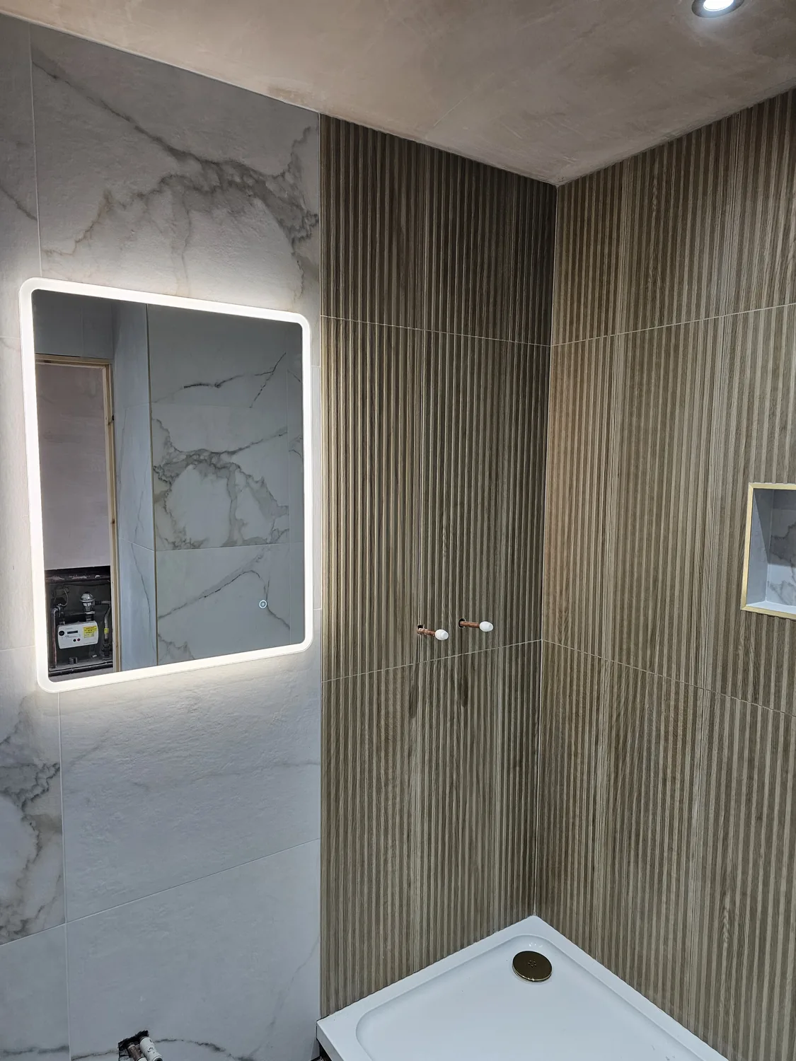 Finished bathroom with large-format marble-effect porcelain, ribbed wood-effect tiling and an illuminated mirror.