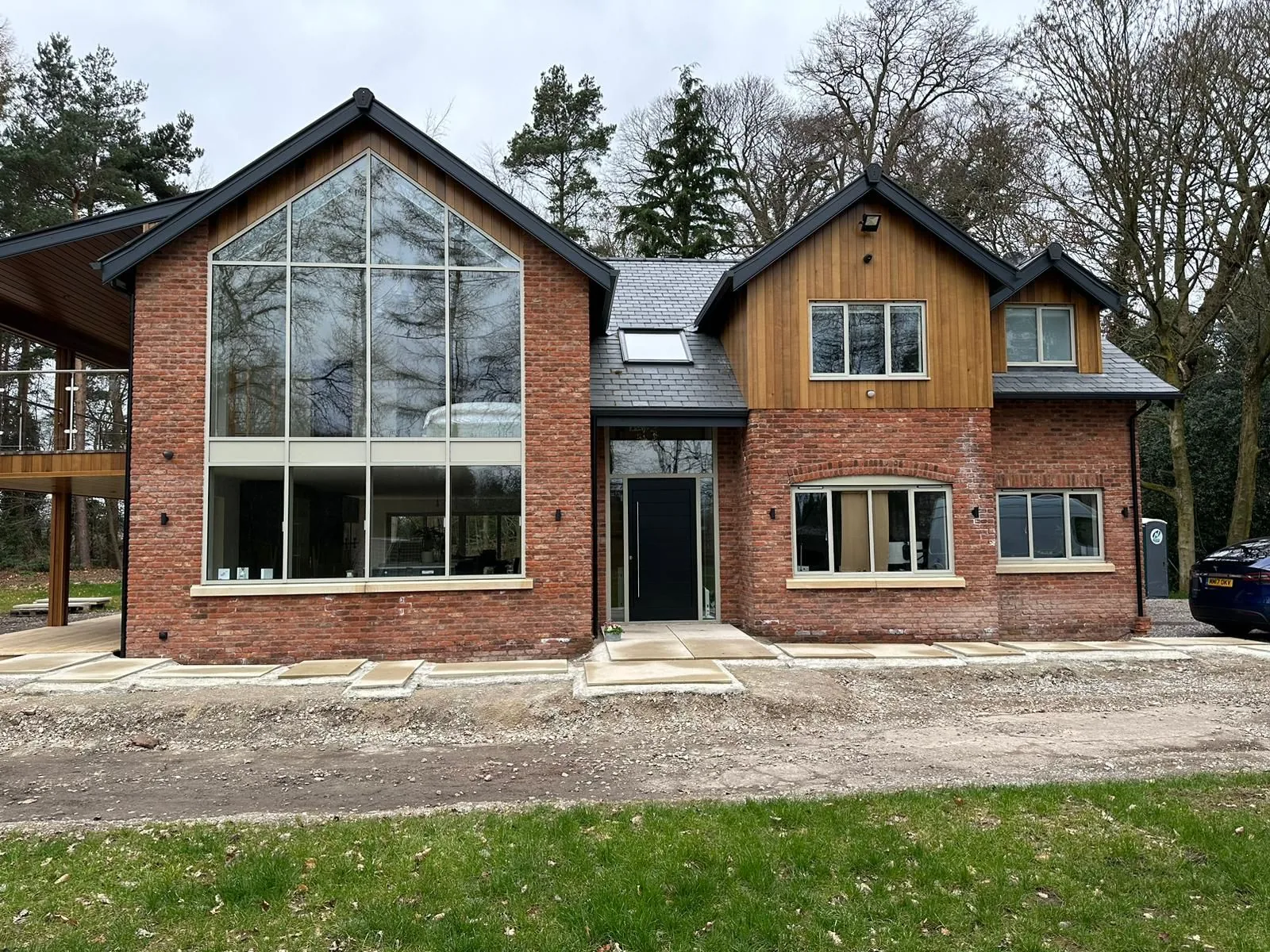 Large brick house with gabled ends, full-height glazing and timber cladding, seen from the garden.