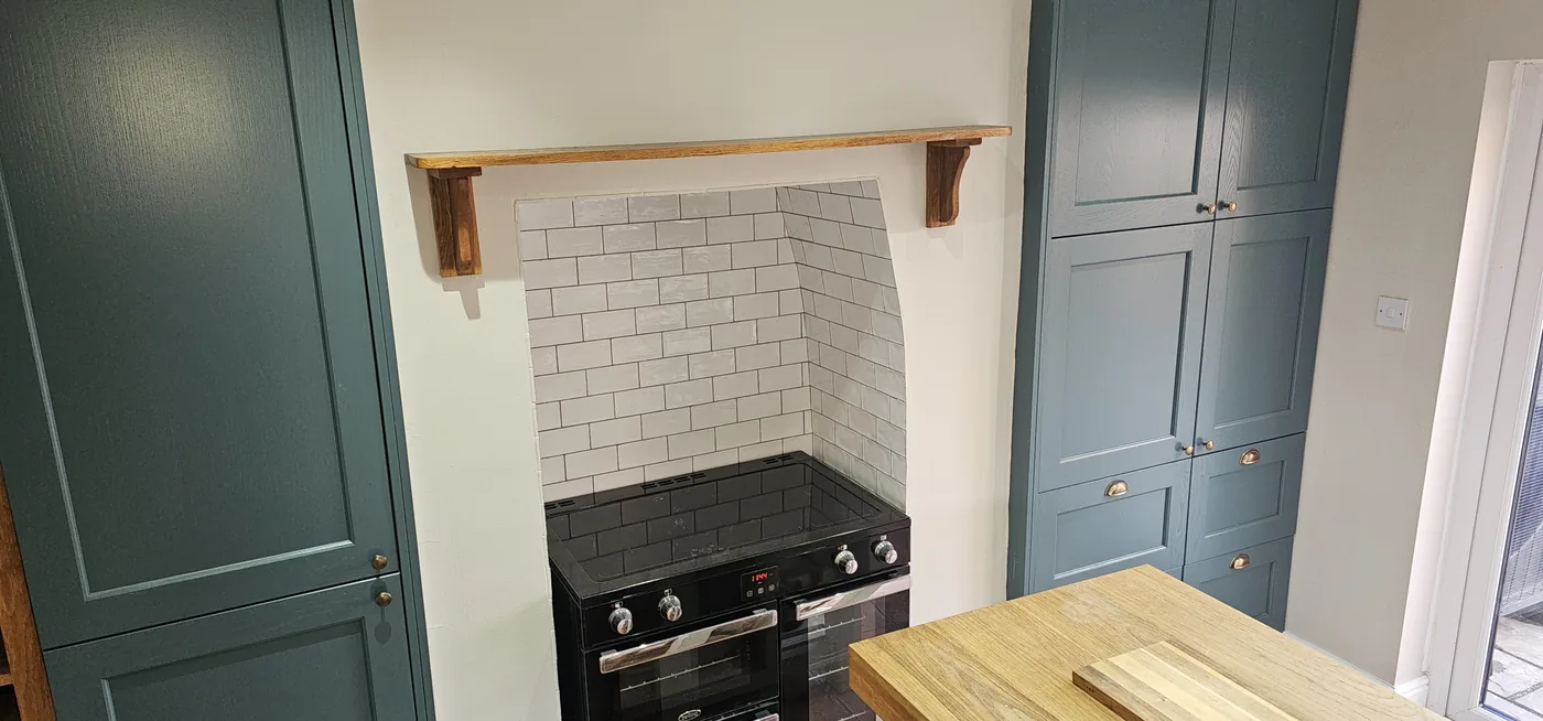 Kitchen with sage green shaker cabinetry, a range cooker in a tiled chimney recess and an oak shelf.