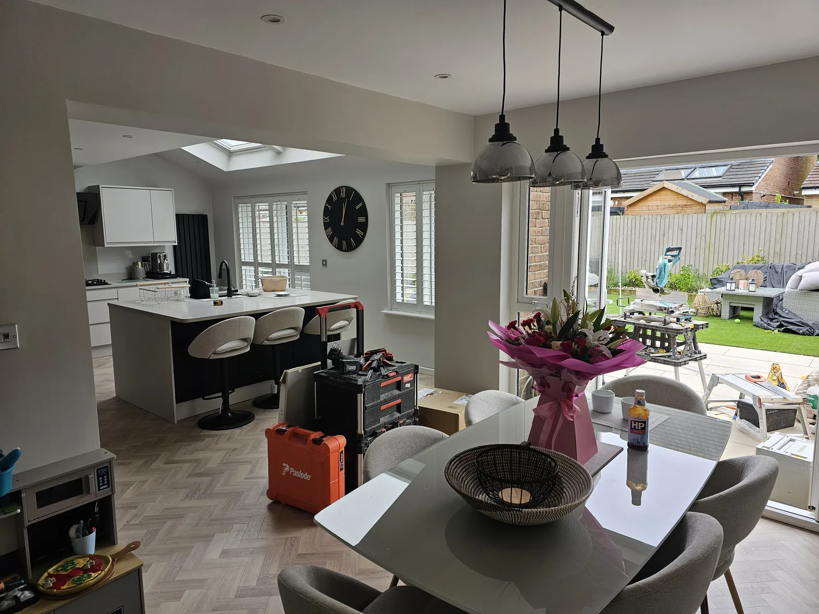 Completed open-plan kitchen and dining room in a rear extension, with a roof lantern, pendant lights over the dining table, plantation shutters and a quartz-topped island.