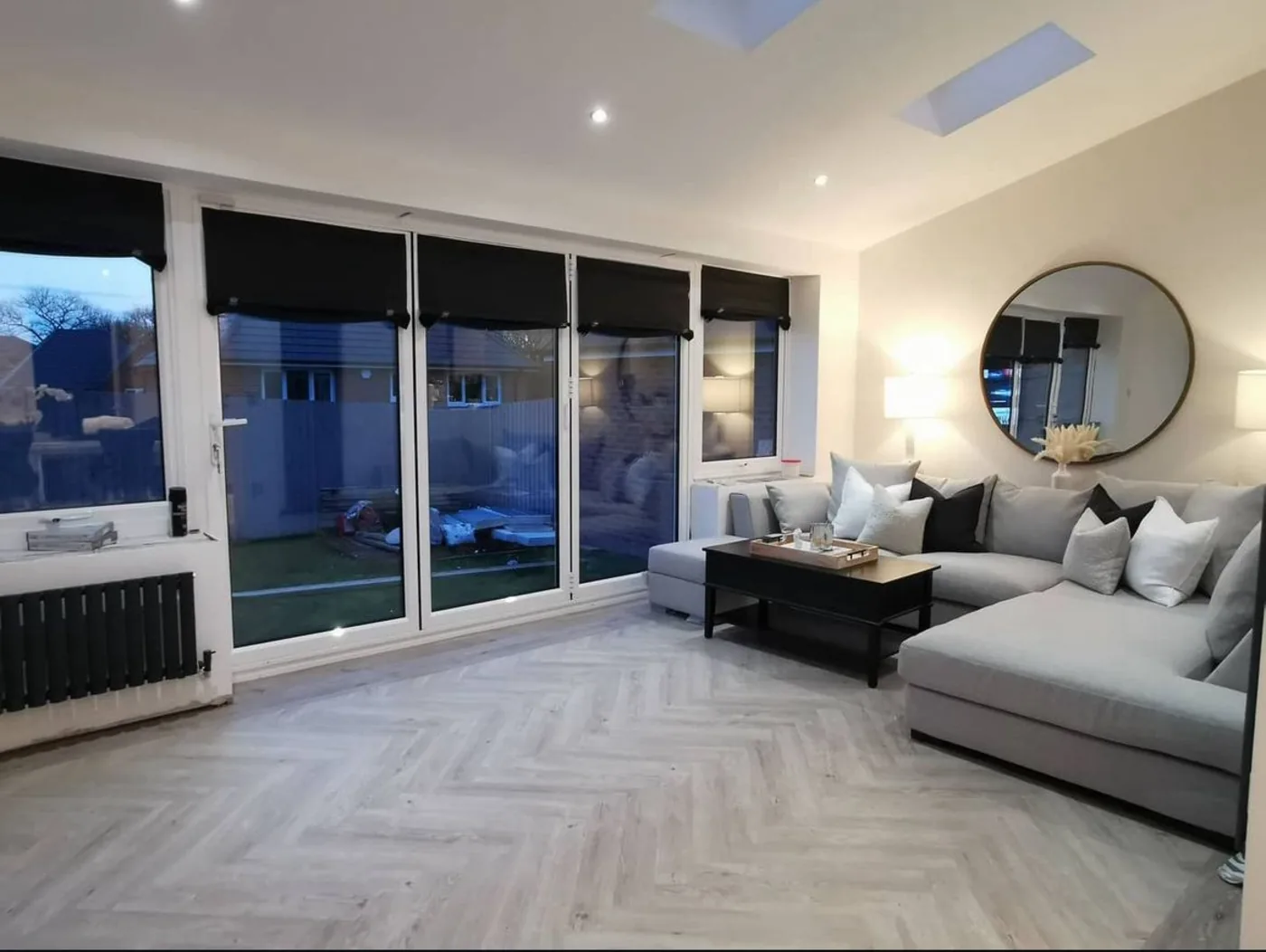 Finished living room with herringbone flooring, full-height sliding doors to the garden and a round wall mirror.