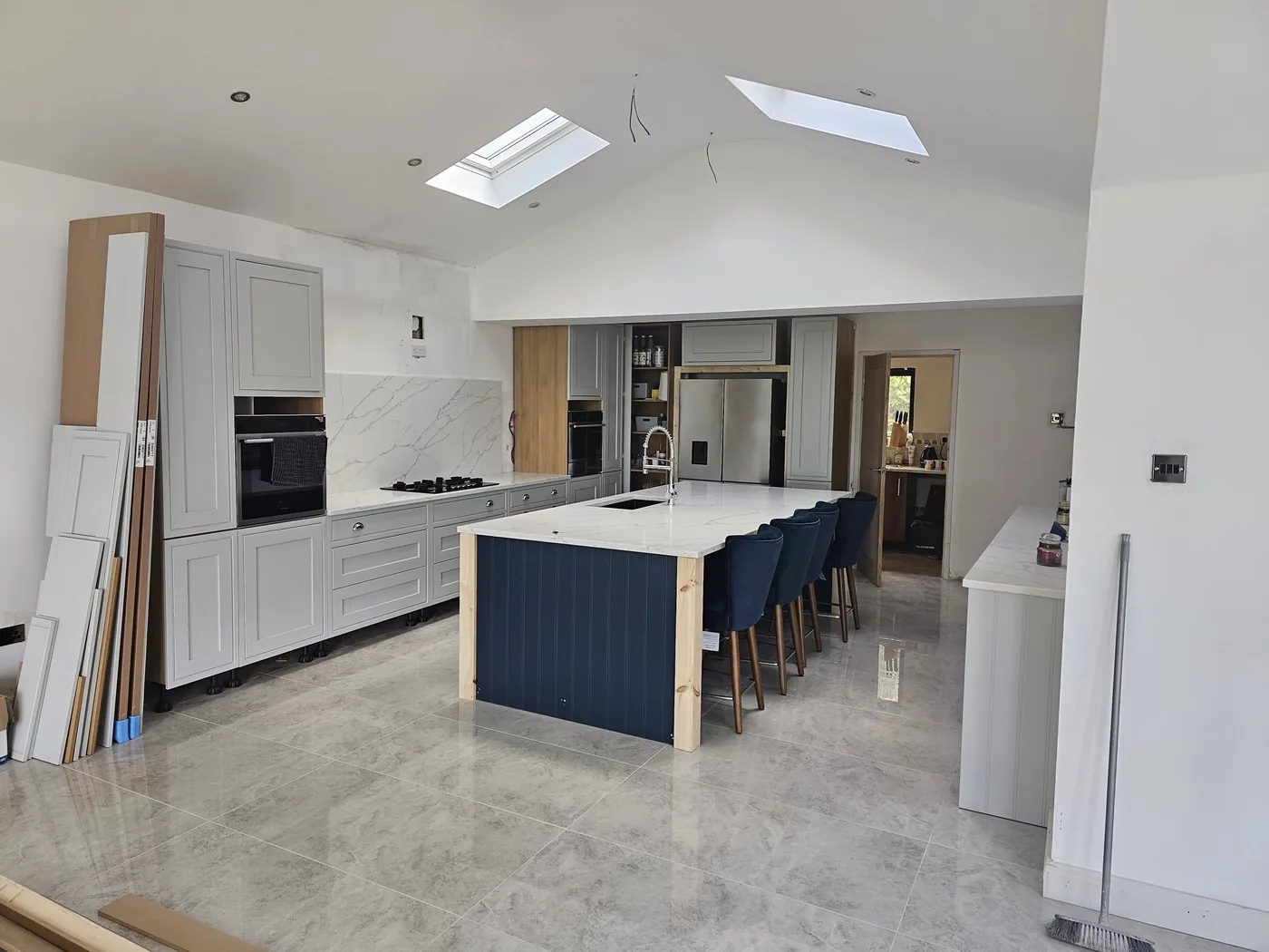 Open-plan kitchen with a navy island, integrated ovens and a full-height marble-effect splashback.