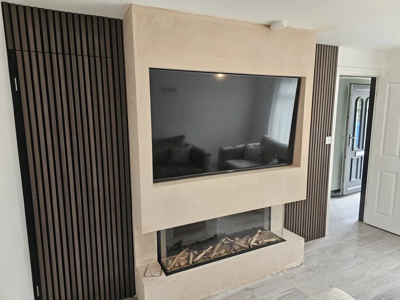 Media wall with an inset linear gas fire, recessed television and vertical oak slatted panelling either side.
