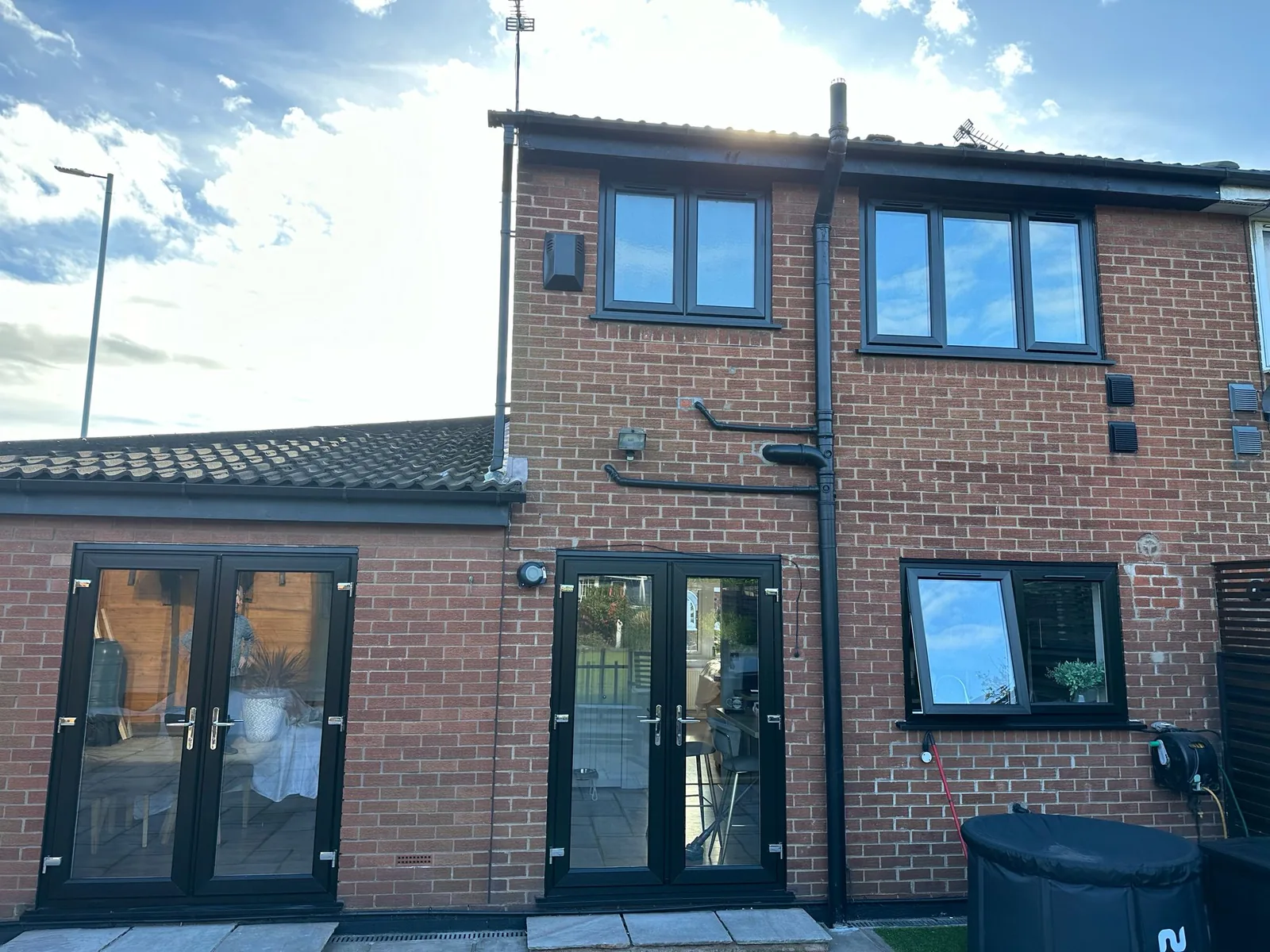 Completed two-storey rear extension in red brick with anthracite grey windows and French doors, and new paving laid up to the threshold.