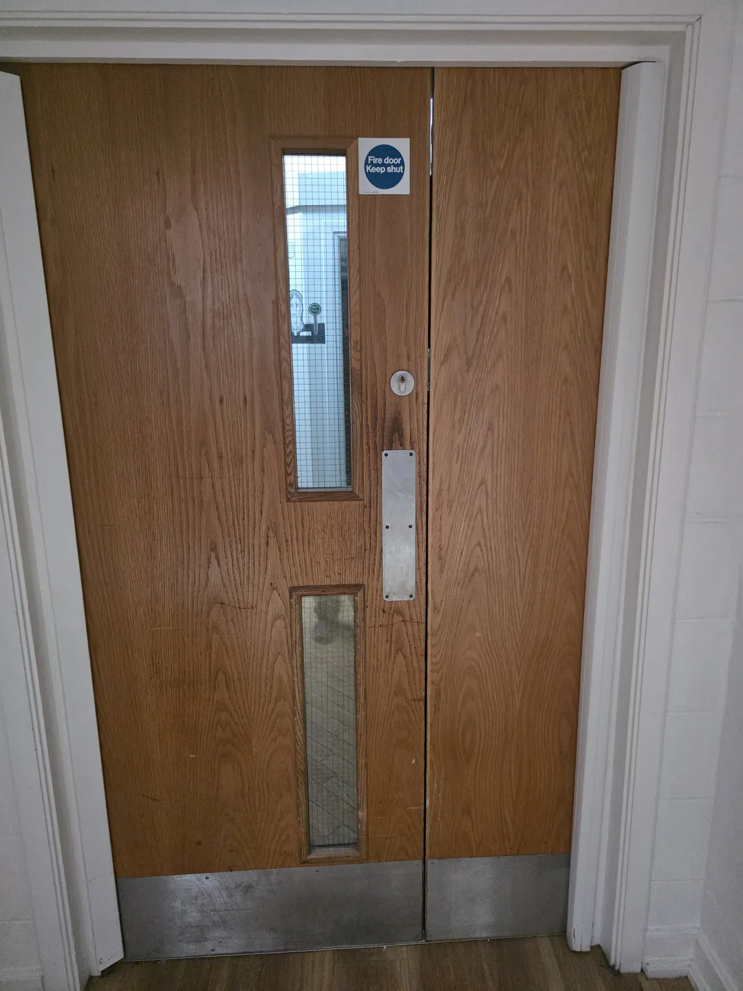 New pair of oak-faced fire doors with vision panels, kick plates and signage in a new opening.
