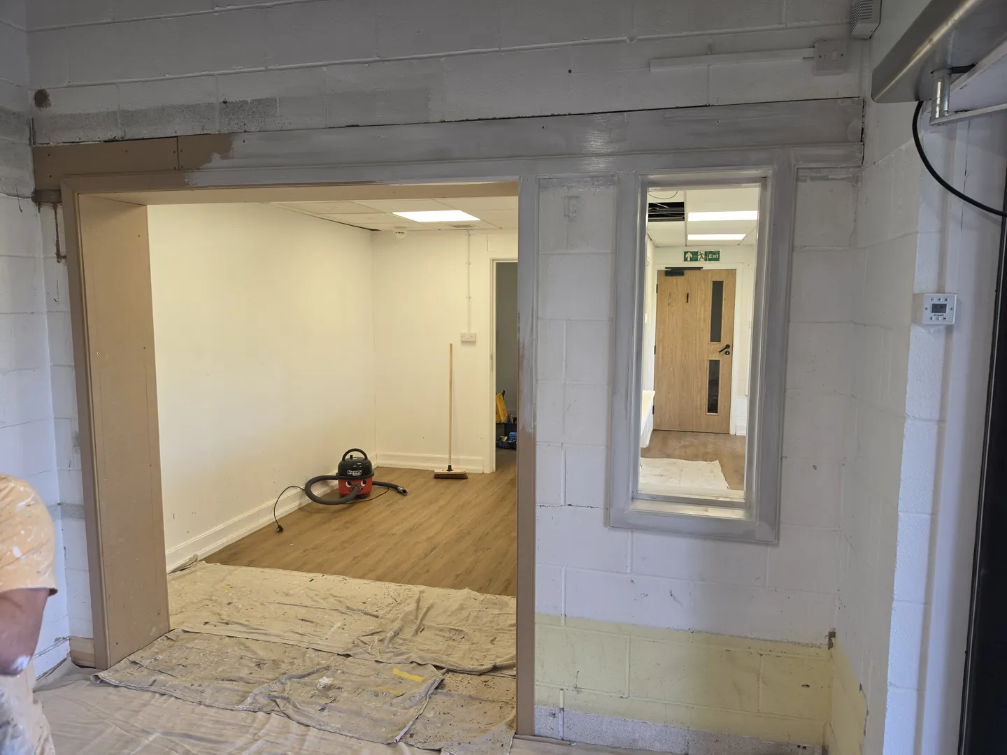 New structural opening with timber linings and a vision panel, looking into a newly decorated room with LVT flooring.