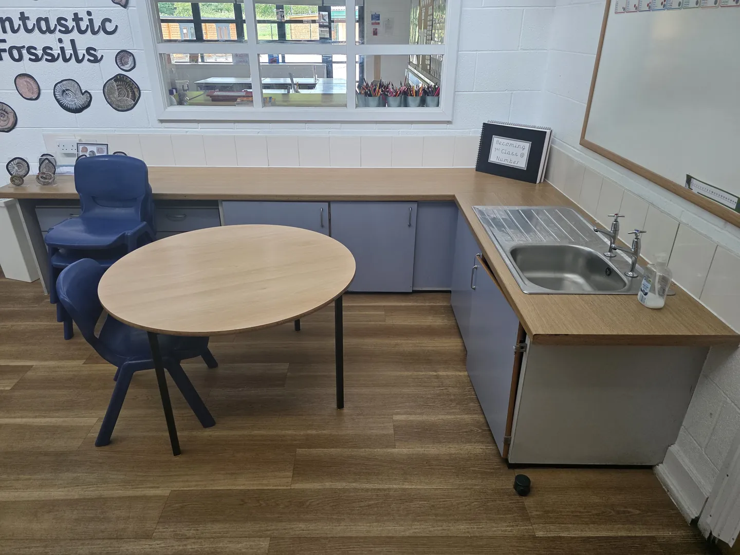 Classroom base with fitted worktop and sink run, wood-effect flooring and a small table and chairs.