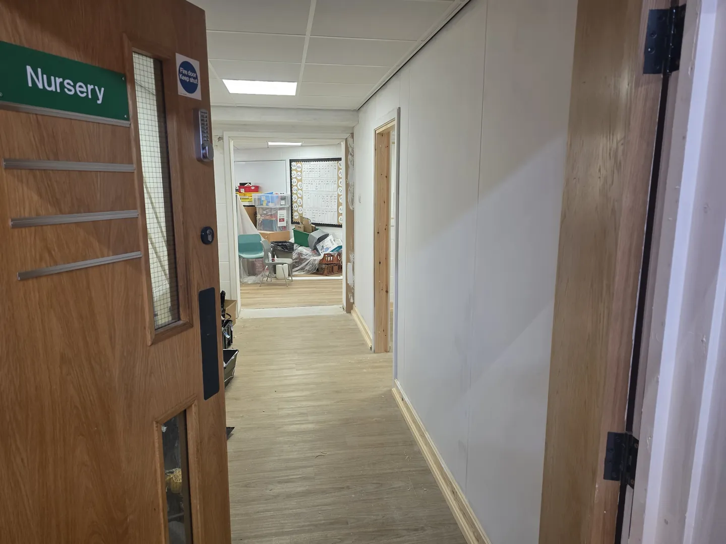 Nursery door opening onto a refurbished corridor with LVT flooring and painted lined walls.