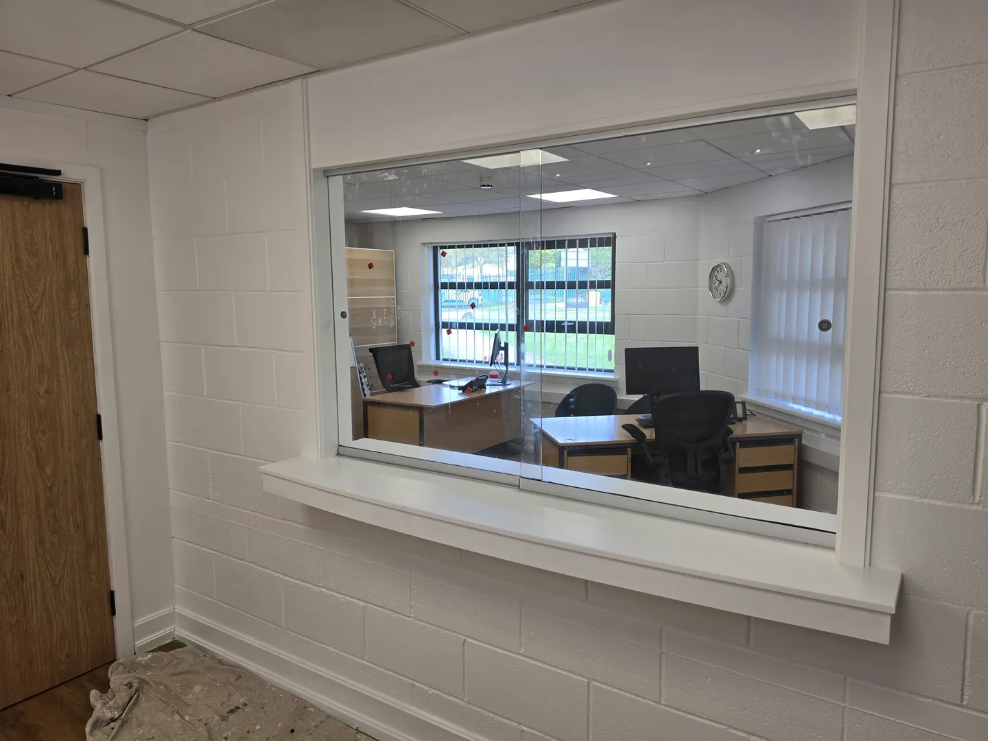 Completed school office servery hatch with a deep white sill, looking through to the refurbished office with desks and new windows.