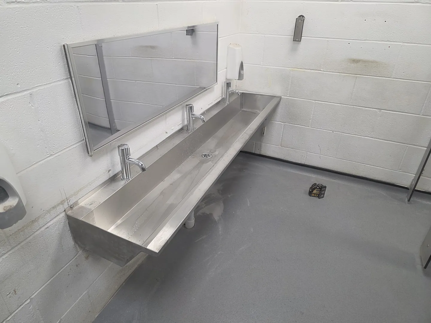 Stainless steel trough basin with mirror and taps fitted in a refurbished washroom with new safety flooring.