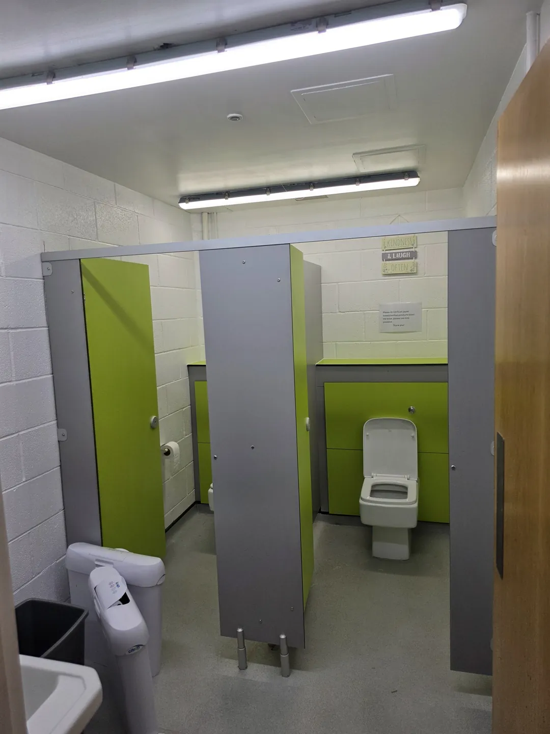 Refurbished school washroom with grey cubicle partitions, a green door and a new toilet.