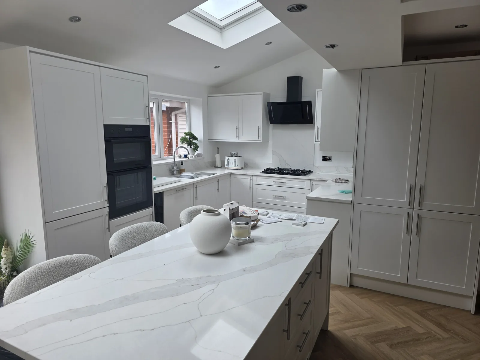 An SJ Developments kitchen with pale shaker cabinets, a marble-effect island and natural light from a rooflight.